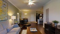 This single-floor residence offers a thoughtfully designed open-concept layout that seamlessly connects the living, dining, and kitchen areas into one cohesive living space. Rich, dark hardwood flooring extends throughout, providing a warm and elegant foundation that ties the interior together.

The living area is generously proportioned, featuring crown molding along the ceilings and a ceiling fan with integrated lighting that adds both comfort and style. The space comfortably accommodates a full seating arrangement, with room for accent furniture and décor.

Adjacent to the living area, the dining space is defined by a classic chandelier overhead, providing ambient lighting for meals and gatherings. A white paneled door serves as the main entry, contributing to the clean, traditional aesthetic of the home.

The kitchen is a functional and stylish hub, equipped with dark cabinetry, a peninsula with bar-height seating, pendant lighting, and a full suite of appliances. Track lighting further illuminates the workspace, making it ideal for everyday cooking and entertaining alike.

Throughout the space, warm, neutral wall tones complement the dark flooring and cabinetry, creating a cohesive and inviting ambiance. The open sightlines between all areas make the home feel expansive and well-connected.