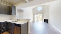Located in Los Angeles, CA, this 2-bedroom, 2-bathroom residence offers a thoughtfully designed layout with modern finishes and architectural character. The living room is a true standout, boasting soaring vaulted ceilings, a distinctive circular clerestory window that floods the space with natural light, a cozy fireplace, and sliding glass doors that open to an outdoor view — all set above rich wood-look flooring. The open kitchen flows seamlessly into the living area and features dark cabinetry, stainless steel appliances including a gas range, microwave, refrigerator, and dishwasher, paired with clean white countertops and a peninsula for added workspace. Both bedrooms are well-proportioned, with the primary bedroom offering generous dimensions, a walk-in closet, and direct access to an en-suite bathroom. The second bedroom benefits from a large window with lush outdoor views. Each bathroom is finished with stylish blue-toned wood-grain vanities, vessel sinks, white quartz countertops, framed mirrors, and a tub-shower combination. Wood-look flooring runs throughout the entire residence, adding warmth and continuity. Dedicated closets in each bedroom provide ample storage across the home.
