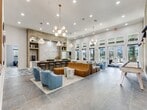 This 1760 square foot single-story space in Austin, TX, showcases a harmonious blend of modern design and functionality. The open-concept layout creates a seamless flow between different areas, each thoughtfully curated for specific purposes.

The main living area boasts high ceilings and large windows, flooding the space with natural light. A striking chandelier with globe-shaped lights serves as a focal point, complementing the room's contemporary aesthetic. The seating arrangement features a unique orange modular sofa and comfortable blue armchairs, perfect for relaxation or social gatherings.

Adjacent to the living area, a sleek kitchen with a large island and bar seating offers a perfect space for casual dining or entertainment. The kitchen's clean lines and minimalist design contribute to the overall modern feel of the space.

A separate area showcases a distinctive accent wall with diagonal white paneling, adding visual interest and texture. This space includes a vibrant yellow chair and a playful oversized Connect Four game, suggesting a recreational or gaming zone.

The entrance area impresses with its high ceilings, chandelier, and glass doors that provide expansive views of the outdoors. A geometric-patterned floor adds a touch of sophistication to this welcoming space.

Additional seating areas throughout the property, including a dining nook with plaid-upholstered chairs, provide versatile spaces for work or leisure. The thoughtful design and contemporary furnishings create an inviting, multifunctional environment suitable for various activities and gatherings.