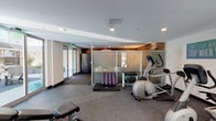 Located at 150 N Berendo St in Los Angeles, this well-equipped fitness center offers a comprehensive range of workout amenities within a thoughtfully designed, single-floor layout. The space features durable rubber flooring throughout, recessed lighting, and a clean, modern aesthetic enhanced by warm wood accent paneling near the ceiling.

The main workout area is home to cardio equipment including an elliptical trainer and stationary bike, along with a multi-use weight bench and a cable machine. A dedicated stretching and yoga zone provides yoga mats and a low platform mat for floor exercises. A compact dumbbell rack with a full range of free weights is neatly organized beside the cardio equipment, separated from the open floor area by frosted glass partition panels that add a sleek, contemporary touch.

A mirrored wall in the secondary workout zone enhances the sense of space and supports form-focused training, accompanied by stability balls and additional strength equipment. Motivational artwork, including a striking large-format photograph of the Hollywood Sign at dusk, adds local character to the environment.

Sliding glass doors lead directly out to a well-appointed outdoor courtyard featuring seating areas, a grill station, and landscaping, providing a seamless indoor-outdoor connection. Package lockers are also accessible from within the fitness center, adding a layer of practical convenience to the space.