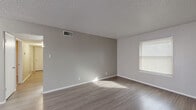 This single-story, 3-bedroom, 2-bathroom home features a clean, neutral aesthetic throughout, with light gray walls, white trim, and a mix of wood-look luxury vinyl plank and plush carpet flooring. The open living room is bathed in natural light through blinds-covered windows, showcasing textured ceilings and seamless access to the hallway connecting all main areas. The galley-style kitchen is well-appointed with gray cabinetry, light stone countertops, a double-basin sink, and black appliances, including a range and refrigerator. An adjacent pantry provides additional storage convenience. The spacious primary bedroom features carpet flooring, a ceiling fan, and a private en suite bathroom equipped with a walk-in shower with sliding glass doors. Two additional bedrooms also feature carpet flooring and natural light from windows with blinds. The shared second bathroom includes a granite-topped vanity with a single sink, a mirrored wall, and a tiled shower-tub combo. Notably, this home offers an exceptional seven closets, ensuring ample storage throughout. A dedicated hallway connects all rooms, providing a logical and efficient floor plan suited for everyday living.
