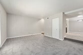 This 1-bedroom, 1-bathroom unit is thoughtfully laid out across a single floor, offering a functional and comfortable living arrangement. The floor plan connects key areas via a series of hallways, providing clear separation between living, sleeping, and utility spaces.

The living room is a generously sized area finished with plush carpet and neutral-toned walls. A set of French doors allows natural light to flow in while offering outdoor access. A textured ceiling is consistent throughout the unit, adding subtle visual character.

The kitchen features hardwood-style flooring, gray cabinetry, light stone-finish countertops, and black appliances including a range and refrigerator. A single-basin sink with a modern faucet completes the efficient galley-style layout.

The bedroom is a spacious, carpeted retreat equipped with a ceiling fan and a window that brings in natural light. It provides direct access to both a closet and the full bathroom, which includes a single-vanity with a light stone countertop, framed mirror, and a tub/shower combination with wood-style flooring. The hallway system connects all areas cohesively, enhancing the overall flow of the unit.