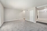 This 1-bedroom, 1-bathroom unit is thoughtfully laid out across a single floor, offering a functional and comfortable living arrangement. The floor plan connects key areas via a series of hallways, providing clear separation between living, sleeping, and utility spaces.

The living room is a generously sized area finished with plush carpet and neutral-toned walls. A set of French doors allows natural light to flow in while offering outdoor access. A textured ceiling is consistent throughout the unit, adding subtle visual character.

The kitchen features hardwood-style flooring, gray cabinetry, light stone-finish countertops, and black appliances including a range and refrigerator. A single-basin sink with a modern faucet completes the efficient galley-style layout.

The bedroom is a spacious, carpeted retreat equipped with a ceiling fan and a window that brings in natural light. It provides direct access to both a closet and the full bathroom, which includes a single-vanity with a light stone countertop, framed mirror, and a tub/shower combination with wood-style flooring. The hallway system connects all areas cohesively, enhancing the overall flow of the unit.