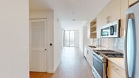 Located at 330 13th St in San Diego's vibrant East Village neighborhood, this modern high-rise unit offers a thoughtfully designed layout with clean lines and contemporary finishes throughout. Light wood-tone flooring flows seamlessly across the main living areas, complementing the bright white walls and creating a cohesive, airy aesthetic.

The galley-style kitchen is efficiently appointed with light wood cabinetry featuring open shelving, a subway tile backsplash, quartz countertops, and a full suite of stainless steel appliances including a gas range, built-in microwave, and refrigerator. A sleek coil-neck faucet adds a modern touch to the undermount sink.

The open living area is a standout feature, highlighted by expansive floor-to-ceiling windows and a sliding glass door that leads to a private balcony. From this elevated vantage point, sweeping views of the San Diego skyline and surrounding cityscape flood the space with natural light throughout the day.

The bathroom is clean and modern, featuring large-format tile flooring, a white vanity with ample storage, and a backlit frameless mirror. Adjacent to the bedroom, a generously sized walk-in closet provides abundant storage with dual hanging rods and built-in shelving. The overall design balances functional urban living with an elevated, contemporary aesthetic.