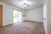 This single-floor home accommodates three bedrooms and one bathroom within a well-utilized floor plan. The living area is anchored by a ceiling fan with light fixture and features sliding glass doors that invite natural light and provide outdoor access. A built-in pass-through with a wood-trimmed ledge connects the living space to an adjacent area, adding a functional architectural detail. Baseboard heating units are present throughout, ensuring consistent warmth.

The spacious primary bedroom includes a ceiling fan, a wall-mounted air conditioning unit, and its own sliding glass door to the exterior. It also features a closet with warm wood-toned sliding doors. The two additional bedrooms each include ceiling fans, carpeted floors, baseboard heaters, and windows with blinds that allow natural light while maintaining privacy. One bedroom also offers closet access.

The full bathroom features a white vanity with sink, a large mirror, a shower/tub combination, and wood-look vinyl flooring. A hallway connects the bedrooms and provides access to an in-unit laundry area with a stacked washer and dryer. Warm wood-toned trim, white walls, and neutral carpeting throughout create a clean, consistent aesthetic across the home.