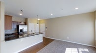 This single-floor residence offers a thoughtfully designed open-concept layout that promotes a natural flow between the kitchen and living areas. The kitchen is a standout feature, anchored by a sleek island with dark countertops and a double basin sink, complemented by stainless steel appliances and dark wood cabinetry. Pendant lighting hangs above the island, adding both style and function to the space. Recessed lighting throughout the ceiling ensures the interior is well-lit and inviting. The flooring transitions smoothly from rich hardwood in the kitchen and entryway to plush carpeting in the living area, creating a warm and comfortable atmosphere. Neutral warm-toned walls provide a versatile backdrop, making the space feel open and airy. Multiple interior doors lead to additional rooms, suggesting a well-organized floor plan with clearly defined private and shared spaces. A wall-mounted smart panel near the entryway adds a modern, connected living touch. Overall, the space combines practical design with contemporary finishes to create a comfortable and functional living environment.