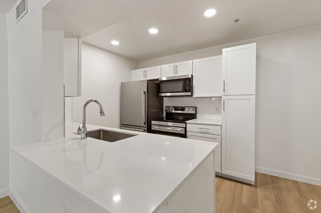 Modern kitchen with sleek white cabinetry, stainless steel appliances, and elegant quartz countertop. - Pointe at North Penn