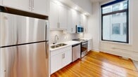 Located on N Ninth Street in downtown Richmond, Virginia, this single-floor unit blends classic character with modern updates. Warm-toned hardwood floors run continuously throughout the living areas and bedroom, lending a cohesive and inviting feel to the entire space. The open-concept layout connects the living area directly to the kitchen, creating a spacious, uninterrupted flow that makes the unit feel particularly generous.

The kitchen is well-appointed with white shaker-style cabinetry, light countertops, a subway tile backsplash, and a full suite of stainless steel appliances, including a refrigerator, range, microwave, and dishwasher. A double-basin sink sits beneath a window, adding practicality to the workspace.

Large, dark-framed windows in both the living area and bedroom admit abundant natural light and provide views of the surrounding urban streetscape. The bedroom is a comfortable size, featuring its own set of oversized windows and a built-in closet. A ceiling fan in the main living area adds to overall comfort.

The bathroom is finished with light tile flooring, a dark wood vanity topped with a granite countertop, a large mirror, and a tub-shower combination. The overall aesthetic throughout the unit is clean, bright, and modernly refreshed while retaining the architectural character of the historic building.