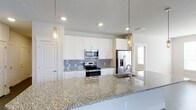 This single-floor space showcases a well-designed, open-concept kitchen that serves as a central highlight. The kitchen features crisp white shaker-style cabinetry that extends to the upper walls, providing ample storage while maintaining a clean, bright aesthetic. Complementing the cabinetry is a light-toned granite countertop with intricate veining, offering generous prep space along the perimeter and a wide island or peninsula with an undermount sink — ideal for both cooking and casual dining.

A gray subway tile backsplash adds a modern, textured contrast against the white cabinets, while stainless steel appliances — including a range, built-in microwave, and French door refrigerator with an in-door water and ice dispenser — contribute to a polished, contemporary look. Two elegant glass pendant lights hang above the island, enhancing the kitchen's visual appeal and providing focused task lighting.

Recessed lighting throughout ensures the space is well-lit, and neutral-toned walls and flooring create a cohesive, airy ambiance. A doorway visible in the background suggests a seamless flow into adjacent living areas, making this a highly functional and inviting space.