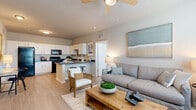 This single-story residence in Brooksville, Florida, offers a thoughtfully designed open-concept layout with a neutral color palette and light wood-style flooring throughout the main living areas. The living room serves as the heart of the home, featuring elevated ceilings, a ceiling fan, and generous natural light streaming through large windows with blinds. The space comfortably accommodates a full seating arrangement and connects seamlessly to the kitchen and dining area.

The kitchen is well-equipped with white cabinetry, dark granite-style countertops, and a full suite of black appliances, including a range, microwave, refrigerator, and dishwasher. A peninsula with bar seating provides additional prep space and casual dining. The open sightlines between the kitchen and living area enhance the sense of spaciousness throughout.

Both bedrooms are carpeted and receive ample natural light through large windows. Each room includes a ceiling fan and closet space. The bathroom features a full tub-shower combination with clean white finishes and chrome fixtures. A dedicated laundry room houses a full-size washer and dryer with built-in wire shelving above, adding practical everyday convenience to the overall layout.
