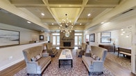 This beautifully appointed lobby exudes a classic, refined charm from the moment you step inside. The focal point of the space is a stunning coffered ceiling, which adds architectural depth and sophistication, complemented by a striking Sputnik-style chandelier that serves as a bold design statement. Recessed lighting throughout ensures the space is warmly and evenly illuminated.

A floor-to-ceiling stone fireplace anchors the far wall, flanked by large windows and glass-panel doors that invite natural light to fill the room. A decorative round mirror rests above the fireplace mantle, further enhancing the space's character.

The seating area is generously arranged with a pair of neutral-toned sofas, accent chairs, and upholstered armchairs, all centered around a rectangular coffee table. An ornate patterned area rug ties the seating arrangement together, adding warmth and visual interest underfoot.

The overall ambiance is inviting and elegant, balancing traditional architectural details — such as the coffered ceiling and stone fireplace — with carefully chosen furnishings. The result is a lobby that feels both grand and comfortable, offering a welcoming first impression that sets a high standard for the rest of the property.