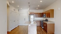 This thoughtfully designed single-floor residence offers a clean, contemporary aesthetic throughout. The kitchen serves as the heart of the home, showcasing rich warm-toned wood cabinetry, speckled granite countertops, and a full suite of stainless steel appliances including a gas range, microwave, and refrigerator. A central island with an integrated sink and stylish glass pendant lighting above adds both functionality and visual appeal. Light hardwood flooring runs throughout the main living areas, enhancing the bright, open atmosphere.

The bedrooms are carpeted for comfort, with one featuring a tray ceiling detail and access to a generously sized walk-in closet outfitted with built-in shelving and double hanging rods. A second bedroom benefits from a window with natural light. A large floor-to-ceiling window in one area of the unit frames views of the surrounding building exterior, allowing abundant daylight to filter in.

The bathrooms are finished with the same speckled granite countertops found in the kitchen. The primary bath includes a dual-sink vanity with brushed nickel fixtures, while the secondary bath offers a single-sink vanity. Recessed lighting throughout and a neutral white color palette lend the entire space a clean, modern, and inviting character.