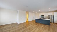 Located at 3900 W Broad St in Richmond, Virginia, this single-floor unit offers a clean, contemporary design with a thoughtful open-concept layout. Warm hardwood-style flooring flows seamlessly throughout the main living areas, creating a cohesive and inviting atmosphere. The expansive living area is bathed in natural light from a bank of large windows fitted with blinds, offering views of the surrounding neighborhood.

The kitchen is a standout feature, anchored by a bold slate-blue island with a white quartz countertop and an integrated sink. Two-tone cabinetry pairs crisp white upper cabinets with dark lower cabinets, complemented by a herringbone tile backsplash and a full suite of stainless steel appliances, including a refrigerator, electric range, and microwave. Recessed lighting above keeps the space bright and functional.

The bedrooms continue the light, airy aesthetic with neutral walls, hardwood-style flooring, and well-sized windows that invite natural light. The bathroom is efficiently appointed with a full tub-shower combination, brushed nickel fixtures and grab bar, tile flooring, and a dark-cabineted vanity. Throughout, the unit presents a fresh, modern finish that is both practical and visually appealing.