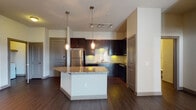 Located at 1350 N Greenville Ave in Richardson, TX, this single-floor residence offers a thoughtfully designed open-concept layout with contemporary finishes throughout. The kitchen serves as a central highlight, showcasing rich dark cabinetry that extends to the ceiling, granite countertops, a classic subway tile backsplash, and a full suite of stainless steel appliances including a refrigerator, range, microwave, and dishwasher. A curved peninsula with pendant lighting provides both additional prep space and a natural transition into the living area. The living room is generously proportioned, featuring rich hardwood-style flooring, a ceiling fan, and a set of French doors that invite natural light and provide access to the outdoors. Track lighting and pendant fixtures add dimension and warmth to the common areas. The bedroom offers plush carpeting and a bright window with blinds, while a spacious walk-in closet with multiple shelving rods provides ample storage. The bathroom is cleanly appointed with a granite-topped vanity, dark cabinetry, hardwood-style flooring, and a glass-enclosed walk-in shower. A dedicated hallway connects the private spaces seamlessly, completing a well-organized and modern floor plan.