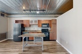 Located at 201 S 1st St in the heart of Ann Arbor, MI, this one-bedroom, one-bathroom loft-style unit offers a thoughtfully designed single-floor layout with a distinctive industrial aesthetic. The space features exposed corrugated metal ceilings with visible ductwork and track lighting throughout, creating a modern urban character that sets it apart.

The open kitchen is well-appointed with warm wood cabinetry, granite countertops, black appliances including a refrigerator, electric range, built-in microwave, and dishwasher, plus a rolling granite-topped kitchen island that adds flexible prep and dining space. Hardwood-style plank flooring runs throughout the main living areas, complementing the loft's industrial character.

A narrow hallway with frosted glass sliding doors connects the living area to the private spaces, offering a sleek, contemporary touch. The bedroom is carpeted for comfort and features the same exposed corrugated ceiling detail, with a small clerestory window allowing in soft natural light. Two closets provide practical storage throughout the unit.

The bathroom includes a wood-framed vanity mirror, vessel sink, and a full shower-tub combination. Additional conveniences include a dedicated laundry area and a utility room. Large windows at the end of the main corridor draw in natural light and frame views of the surrounding downtown streetscape.