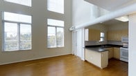 Located at 4021 Falcon in San Diego, this two-story loft offers a striking open-concept design defined by dramatic double-height ceilings that immediately create a sense of expansiveness and volume. Large windows along the main living area flood the space with natural light, offering views of surrounding greenery and enhancing the bright, airy atmosphere throughout.

The main level seamlessly integrates the living area with a functional kitchen, which features light wood cabinetry, dark countertops, and a peninsula that provides additional workspace and serves as a natural divider between the cooking and living zones. An exposed ventilation duct adds an industrial character to the space, complementing the clean, modern aesthetic.

Warm wood-tone flooring runs throughout the main level, adding warmth and continuity to the open layout. The neutral wall palette keeps the space versatile and easy to personalize. The two-floor configuration provides a natural separation between living and private areas, offering both openness on the main level and a more intimate upper level typical of loft-style design. Overall, this loft delivers a compelling blend of modern industrial aesthetics and practical functionality in a well-located San Diego address.