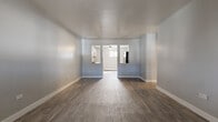 This single-floor unit offers a clean, updated interior designed for comfortable everyday living. The open living area is finished with durable luxury vinyl plank flooring in a warm gray-brown tone, complemented by light blue-gray walls and crisp white baseboards that give the space a fresh, modern feel. Two pass-through openings connect the living area to the adjacent kitchen and dining space, maintaining an open and airy flow throughout.

The kitchen is thoughtfully renovated, featuring white shaker-style cabinetry, granite-look countertops, a subway tile backsplash, and a stainless steel sink. Black appliances, including a gas range and over-the-range microwave, provide a practical contrast to the bright cabinetry. The kitchen also benefits from its own vinyl plank flooring, consistent with the main living areas.

The bedrooms are carpeted with neutral-toned plush carpet, offering a softer underfoot experience. Each room is finished with the same light gray wall palette and white trim. Windows dressed with vertical blinds allow for natural light and privacy. Baseboard heaters are present throughout the unit, and a wall-mounted air conditioning unit is also featured, ensuring year-round climate comfort. The overall layout, as seen in the dollhouse view, is compact yet efficient, with well-defined spaces that maximize functionality.