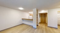 Located at 5335 SW Murray Blvd in Beaverton, Oregon, this single-floor, one-bedroom unit offers a functional and well-organized layout. The entrance opens into a bright, open-concept living and kitchen area finished with light wood-look hard-surface flooring. The kitchen is equipped with a white electric range, a full-size refrigerator, and warm wood-toned cabinetry, all accessible via a peninsula counter with a dark laminate top that doubles as a breakfast bar. Open shelving adjacent to the kitchen provides additional storage, complemented by a separate pantry space. The living area is spacious relative to the unit's overall footprint, featuring a wall-mounted PTAC heating and cooling unit and a window with vertical blinds that invites natural light. The bedroom is carpeted for comfort, features a sliding closet door, and includes a window with greenery views. The bathroom is outfitted with a full tub-shower combo, grab bars for safety and accessibility, and neutral tile surrounds. Throughout the unit, textured ceilings, flush lighting fixtures, and clean white walls contribute to a simple, functional aesthetic well-suited for everyday living.
