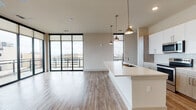 This contemporary 2-bedroom, 2-bathroom residence in Memphis, TN offers a thoughtfully designed open-concept layout with hardwood-style flooring throughout. The living and dining area is anchored by dramatic floor-to-ceiling windows with black framing, flooding the space with natural light and providing sweeping views of the Memphis skyline and the Mississippi River. A private balcony extends the living space outdoors. The kitchen is well-appointed with white cabinetry, stainless steel appliances including a refrigerator, range, and microwave, along with a large waterfall-edge island illuminated by stylish brass pendant lights — ideal for both cooking and entertaining. Each bedroom is generously sized, featuring ceiling fans, warm neutral tones, and large windows with city views. The primary bathroom offers a granite-topped double vanity, wood-toned cabinetry, and a glass-enclosed walk-in shower with white tile surround. The second bathroom includes a tiled soaking tub and shower combination with clean, modern finishes. A walk-in closet is accessible from the secondary bath. The overall aesthetic is clean and modern, blending contemporary design with functional living in the heart of downtown Memphis.