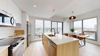 Located at 1240-1250 Cummings Ave in Ottawa, this modern 2-bedroom, 1-bathroom unit offers a thoughtfully designed open-concept layout finished with light hardwood flooring and crisp white walls throughout. The combined kitchen, dining, and living area forms the heart of the space, anchored by a striking kitchen island with a quartz countertop, warm light wood cabinetry, a matte black faucet, and stainless steel appliances including a built-in microwave, range, and full-size refrigerator. A white tile backsplash and recessed lighting complete the kitchen's clean, contemporary aesthetic. Floor-to-ceiling windows in the dining and living areas flood the space with natural light and frame expansive city views, with direct access to a balcony. The living room is comfortably proportioned with high ceilings and a relaxed, airy feel. The primary bedroom features a large window with panoramic views and a sliding door closet, while the second bedroom is bright and well-sized. The bathroom includes a soaking tub, a vanity with mirrored medicine cabinet, and gold-accented shelving details. A dedicated closet and in-unit laundry add to the functional appeal of this well-appointed urban residence.