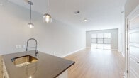 Located at 547–553 Berkley Pkwy in Kansas City, Missouri, this single-floor residence offers a thoughtfully designed open-concept layout with clean, contemporary finishes throughout. Light hardwood flooring runs seamlessly through the main living areas, reflecting natural light and lending a bright, airy feel to the space.

The kitchen is a standout feature, equipped with stainless steel appliances including a range, microwave, and refrigerator. White cabinetry extends to the ceiling for generous storage, complemented by dark stone countertops and a light blue subway tile backsplash. A center island with pendant globe lighting serves as both a functional workspace and a visual focal point that connects the kitchen to the open living area.

The spacious living area flows naturally toward large sliding glass doors and wide windows fitted with horizontal blinds, inviting ample natural light and providing access to outdoor views. Recessed lighting throughout the main areas adds to the bright, modern atmosphere.

The bedroom features soft carpeting, a ceiling fan, and a window that brings in natural light. The bathroom is well-appointed with a dual-sink vanity, dark stone countertops, white cabinetry, framed mirrors, and a full tub-shower combination with tiled surround. Additional closet space is also available within the unit, providing practical storage solutions throughout.
