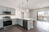 This well-appointed one-bedroom, two-bathroom residence offers a thoughtfully designed single-floor layout that maximizes functionality and modern style. The open-concept kitchen serves as the heart of the home, featuring gray shaker cabinetry, white quartz countertops, a classic subway tile backsplash, and a full suite of stainless steel appliances including a refrigerator, range, microwave, and dishwasher. A peninsula with pendant lighting extends into the living area, creating a natural space for dining or entertaining. Sliding glass doors lead to a private balcony, filling the living area with natural light and offering views of the surrounding cityscape.

The primary bedroom is a comfortable retreat, finished with plush carpeting and a window framing pleasant outdoor views. Two bathrooms serve the unit: one features a marble-tiled walk-in shower, a quartz-top vanity, and modern light fixtures, while the second offers a clean, understated design with a single vanity and mirror. A dedicated laundry closet houses a stacked washer and dryer, along with the water heater and HVAC system, keeping utilities neatly contained. Dark hardwood-style flooring flows throughout the main living areas, tying the contemporary design together cohesively.