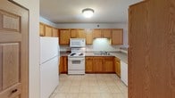 This single-floor residential unit offers a well-organized layout designed for comfortable everyday living. The spacious living room serves as the heart of the home, anchored by a striking terracotta accent wall and a wood-trimmed fireplace that adds warmth and visual interest. Natural light filters in through windows with blinds, and plush carpeting extends throughout the main living and bedroom areas, adding a cozy feel underfoot.

The kitchen is efficiently arranged in a U-shaped configuration, outfitted with warm oak cabinetry, ample counter space, and white appliances including a refrigerator, electric range with microwave above, and dishwasher. Light tile flooring keeps the area practical and easy to maintain. A peninsula counter connects the kitchen to the open living and dining area, creating a natural flow between spaces.

The bedrooms are generously proportioned, each featuring ceiling fans with light fixtures, carpeted floors, and wood-paneled six-panel doors. Baseboard heating and windows with blinds ensure year-round comfort and privacy. The bathroom is clean and functional, featuring a single-basin vanity with oak cabinetry below, a wide mirror, and a well-lit vanity light strip. Tile flooring and neutral tones throughout lend a consistent, understated aesthetic to the entire unit.