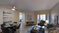 This single-floor residence offers a thoughtfully designed layout that balances comfort and functionality. The open-concept living and dining area serves as the heart of the home, featuring warm hardwood-style flooring, neutral-toned walls, and a ceiling fan that enhances airflow and comfort. A large sliding glass door floods the space with natural light and provides direct access to a private outdoor balcony, offering pleasant views of the surrounding exterior. The living area is generously proportioned, comfortably accommodating both a seating arrangement and a dining set, making it ideal for both relaxing and entertaining. A tasteful media console anchors the space between the living and dining areas. Adjacent to the main living space, the galley-style kitchen is efficiently arranged and well-equipped with stainless steel appliances, including a gas range with oven, over-the-range microwave, and refrigerator. Light wood cabinetry lines the upper and lower walls, complemented by dark granite-style countertops that provide ample workspace. Overhead flush-mount lighting ensures the kitchen is bright and functional. A hallway leads from the living area to the bedroom, which is visible through an open doorway and features the same warm flooring and a tranquil, restful ambiance. The overall design is clean, modern, and move-in ready.