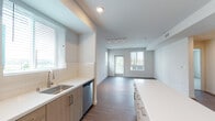 Located at 6825 Alabama Ave in the Canoga Park neighborhood of Los Angeles, this modern single-floor residence offers a clean, contemporary design throughout. The open-concept living and kitchen area is anchored by rich wood-tone flooring and bright white walls, creating a welcoming, light-filled atmosphere. Large windows fitted with horizontal blinds allow abundant natural light to flow through the space, with views of surrounding greenery.

The kitchen is a standout feature, boasting light wood cabinetry, a spacious central island with a crisp white quartz countertop, a full suite of stainless steel appliances including a refrigerator, range, microwave, and dishwasher, and a classic white subway tile backsplash. The living area extends comfortably from the kitchen and opens to a private exterior door, ideal for bringing in outdoor light and air.

The bedrooms are carpeted for comfort and feature sliding-door closets, neutral tones, and windows that overlook the surrounding neighborhood. The bathroom is finished with large-format neutral tile surrounding a full soaking tub and shower combination. In-unit stacked laundry is also included, adding everyday convenience to this thoughtfully designed modern residence.