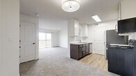 This single-floor, 3-bedroom, 1-bathroom unit offers a functional and well-appointed layout designed to maximize everyday livability. The open-concept kitchen and living area form the heart of the home, where light-toned carpet flows through the living space and transitions to wood-look luxury vinyl plank flooring in the kitchen. The kitchen is equipped with stainless steel appliances — including a range, microwave, and refrigerator — complemented by two-tone cabinetry featuring white upper cabinets and dark lower cabinets, as well as light granite-style countertops and a stainless steel sink. A textured ceiling and flush-mount lighting illuminate the space throughout. The living area is bright and airy, benefiting from a sliding glass door that opens to a private balcony with exterior views. Each of the three bedrooms features plush carpeting, white walls, and ample natural light from sliding or standard windows. The primary bedroom offers a comfortable footprint suited for a full bedroom suite. The full bathroom includes a shower-tub combo, a dark-cabinetry vanity with a white countertop, and wood-look flooring, maintaining a consistent design aesthetic. A connecting hallway ties all rooms together efficiently, creating a cohesive and practical floor plan.