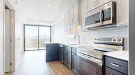 This well-appointed single-floor residence offers a thoughtfully designed layout that balances contemporary aesthetics with functional living. The kitchen serves as a standout feature, showcasing a striking two-tone cabinet design with dark lower cabinets and crisp white upper cabinetry, complemented by a classic white subway tile backsplash, light quartz countertops, and a full suite of stainless steel appliances including a range, over-the-range microwave, dishwasher, and refrigerator. Warm hardwood-style flooring runs throughout the main living and kitchen areas, adding a sense of continuity and warmth.

The living area benefits from an abundance of natural light, with large floor-to-ceiling sliding glass doors that open to a private balcony. From here, expansive views of the city skyline and lush tree canopy can be enjoyed, making the outdoor space a notable highlight of the unit.

The bedrooms are finished with neutral-toned carpet and feature large windows that frame verdant outdoor views, filling each room with natural light. Sliding interior doors provide a sleek, space-conscious touch. Throughout the unit, clean white walls and modern trim create a bright, move-in-ready environment with a polished, contemporary character.