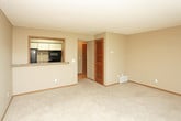 This single-floor residential space offers a practical and comfortable layout with a cohesive, neutral design throughout. The galley-style kitchen is efficiently arranged with white cabinetry, granite-look laminate countertops, a stainless steel sink, and black appliances including a refrigerator, dishwasher, and built-in microwave. Light hardwood-style flooring runs underfoot, and ample upper and lower cabinet storage keeps the space organized.

The living area is generously sized, featuring soft wall-to-wall carpeting in a warm beige tone and neutral taupe walls that create a calm, inviting atmosphere. A large sliding glass door floods the room with natural light and offers a view of the outdoors, complemented by vertical blinds for privacy. A textured ceiling adds subtle character to the space.

A louvered closet door off the main living area provides convenient storage access. The full bathroom includes a tiled shower-tub combination with chrome fixtures, a wood-framed vanity with granite-look countertops, and overhead lighting. Warm wood-toned doors and trim carry throughout the unit, tying the interior design together with a consistent, traditional aesthetic.