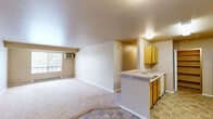 Located at 1636 S Main St in Moscow, Idaho, this two-bedroom, one-bathroom residence offers a functional and well-organized single-floor layout. The open-concept kitchen and living area forms the heart of the unit, where warm honey-toned cabinetry, a peninsula with a sink, and tile-style flooring define the kitchen space. White appliances including a refrigerator, electric range, and microwave are neatly integrated. The living room extends from the kitchen, featuring soft carpet, a wall-mounted air conditioning unit, and a window that brings in natural light. Both bedrooms are carpeted and finished in neutral tones, with the primary bedroom offering a generous walk-in closet equipped with dual hanging rods for ample storage. The second bedroom includes a window with outdoor views and a baseboard heater. The full bathroom features a wide vanity with wood cabinetry, a large mirror, tile-style flooring, and a shower-tub combination. A dedicated laundry area includes built-in shelving alongside a water heater, adding convenience to daily living. Two closets throughout the unit provide additional storage options, making this a practical and comfortable home in the heart of Moscow, Idaho.