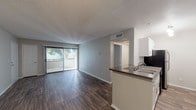 Located at 23645 Meadowridge Dr in Santa Clarita, CA, this single-story residence offers a thoughtfully designed open-concept layout that seamlessly connects the kitchen, dining, and living areas. Rich wood-style flooring runs throughout the main living spaces, complementing the neutral gray walls and textured ceilings.

The kitchen is well-appointed with crisp white cabinetry, dark countertops, a built-in sink on the peninsula, and black appliances including a gas range, over-the-range microwave, and refrigerator. The peninsula provides additional prep and serving space while maintaining an open sightline to the rest of the unit. Adjacent to the kitchen, the dining area features a ceiling fan with light fixture, adding both comfort and functionality.

The spacious living room benefits from abundant natural light streaming through large sliding glass doors fitted with vertical blinds, which open directly to an outdoor patio—ideal for enjoying Southern California's climate. A separate bedroom offers plush carpeting and warm neutral tones, providing a quiet and comfortable retreat. The bathroom is finished with white cabinetry, dark countertops, chrome hardware, a large vanity mirror, and a full tub/shower combo with wood-style flooring throughout.