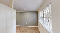 This efficiently designed single-floor unit comprises a living room, kitchen, and bathroom, offering a well-organized and functional layout. The living room is finished with warm wood-look laminate flooring and features cool-toned sage-gray walls accented by crisp white crown molding and baseboards. Recessed lighting illuminates the space, while a large window fitted with white horizontal blinds allows natural light to fill the room, creating a bright and welcoming atmosphere. The galley-style kitchen is thoughtfully appointed with white cabinetry, gray subway tile backsplash, and dark countertops. Stainless steel appliances — including a gas range, dishwasher, and refrigerator — provide modern functionality, while a window above the sink brings in additional natural light. Light-toned ceramic tile flooring completes the kitchen's clean aesthetic. The bathroom maintains a consistent white color palette with a white vanity and sink, a large mirror, and a tiled shower-tub combination. A frosted window provides privacy while allowing soft natural light into the space. Built-in shelving adds a practical storage element. Overall, the unit presents a cohesive, neutral design with modern finishes throughout, making it a practical and move-in ready space.