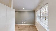 This efficiently designed single-floor unit comprises a living room, kitchen, and bathroom, offering a well-organized and functional layout. The living room is finished with warm wood-look laminate flooring and features cool-toned sage-gray walls accented by crisp white crown molding and baseboards. Recessed lighting illuminates the space, while a large window fitted with white horizontal blinds allows natural light to fill the room, creating a bright and welcoming atmosphere. The galley-style kitchen is thoughtfully appointed with white cabinetry, gray subway tile backsplash, and dark countertops. Stainless steel appliances — including a gas range, dishwasher, and refrigerator — provide modern functionality, while a window above the sink brings in additional natural light. Light-toned ceramic tile flooring completes the kitchen's clean aesthetic. The bathroom maintains a consistent white color palette with a white vanity and sink, a large mirror, and a tiled shower-tub combination. A frosted window provides privacy while allowing soft natural light into the space. Built-in shelving adds a practical storage element. Overall, the unit presents a cohesive, neutral design with modern finishes throughout, making it a practical and move-in ready space.