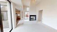This well-appointed two-story home offers a generous and thoughtfully designed layout across two floors. The main level is anchored by a dramatic, open-concept living room boasting soaring two-story ceilings, abundant natural light from high clerestory windows, and a striking floor-to-ceiling fireplace with black tile surround that serves as a bold architectural focal point. Soft carpet flooring and crisp white walls lend the space a bright, airy ambiance throughout.

The kitchen is outfitted with light wood cabinetry, a central island with bar seating, stainless steel appliances including a refrigerator and built-in microwave, and stone tile flooring that extends through the main living areas. A dedicated laundry room includes a full-size washer and dryer with overhead cabinetry for added storage.

The spacious primary bedroom features sliding glass doors opening to a private patio, while the en-suite bathroom includes a dual-sink vanity, a soaking tub set in a tiled niche, stone tile flooring, and generous mirror and vanity lighting. A second bedroom provides convenient access to the kitchen area. Upstairs, a loft adds flexible living space. The home also includes an attached garage, completing this functional and comfortable layout.