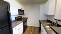 This two-story, one-bedroom, one-bathroom home with loft offers a practical and well-organized layout across two levels. The kitchen features a galley-style design with white cabinetry lining both sides, providing generous storage space. Dark countertops contrast cleanly against the white cabinets, while black appliances — including a gas range, over-the-range microwave, dishwasher, and sink — create a cohesive, modern look. Warm wood-look flooring runs throughout the kitchen, adding texture and a welcoming feel to the space.

The two-floor layout allows for a clear distinction between living and sleeping areas, with the loft offering flexible use as a bedroom, home office, or additional lounge space. The clean, neutral color palette throughout the home creates a bright and open atmosphere, making it easy to personalize with furnishings and décor. Overall, this space combines functional design with a straightforward layout, making it well-suited for individuals or couples seeking a compact yet multi-dimensional living environment.