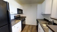This two-story, one-bedroom, one-bathroom home with loft offers a practical and well-organized layout across two levels. The kitchen features a galley-style design with white cabinetry lining both sides, providing generous storage space. Dark countertops contrast cleanly against the white cabinets, while black appliances — including a gas range, over-the-range microwave, dishwasher, and sink — create a cohesive, modern look. Warm wood-look flooring runs throughout the kitchen, adding texture and a welcoming feel to the space.

The two-floor layout allows for a clear distinction between living and sleeping areas, with the loft offering flexible use as a bedroom, home office, or additional lounge space. The clean, neutral color palette throughout the home creates a bright and open atmosphere, making it easy to personalize with furnishings and décor. Overall, this space combines functional design with a straightforward layout, making it well-suited for individuals or couples seeking a compact yet multi-dimensional living environment.