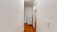Located at 11 Tetlow St, Unit 19 in Boston's Fenway neighborhood, this one-bedroom, one-bathroom unit offers a practical and well-organized layout across a single floor. Warm hardwood floors run throughout the living areas, hallway, and bedroom, giving the unit a consistent and classic character. The living room is a standout space, featuring a charming bay window with decorative leaded glass transoms that allow ample natural light to fill the room. A separate bedroom is well-sized and includes its own window with natural light, a cast-iron radiator for heating, and access to two closets, providing generous storage. The kitchen is equipped with warm-toned wood cabinetry, light countertops, and a window that brings in additional daylight. A white range and full-size refrigerator are included. A narrow hallway connects the rooms efficiently, with the refrigerator tucked at the end near the kitchen entrance. The bathroom features full tile walls and flooring, a soaking bathtub with a shower curtain rod, and a window for ventilation. Classic white trim and molding are found throughout the unit, reflecting the building's traditional New England architectural character.