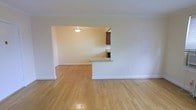 This single-floor residence offers a clean, functional layout with a welcoming open-concept design. The living area is finished with gleaming light hardwood floors that extend throughout, reflecting natural light and lending warmth to the interior. Crisp white walls and bright baseboard trim contribute to a fresh, airy ambiance throughout the space.

A defining architectural feature is the open pass-through connecting the living area to the kitchen. This thoughtfully designed cutout is framed by a half-wall with a granite-topped breakfast bar, providing both a visual connection between the two spaces and a convenient surface for casual dining or entertaining. A pendant light fixture above the pass-through adds a subtle decorative touch while ensuring the area remains well-lit.

The kitchen, visible through the pass-through, features dark wood cabinetry that contrasts nicely with the lighter tones of the surrounding space, and the granite countertops add a touch of elegance to the functional cooking area.

Overall, the space is characterized by its cohesive design, the continuity of the hardwood flooring, and the seamless flow between the living and kitchen areas. The neutral color palette and clean lines make it a versatile and inviting environment suitable for a variety of interior styles.
