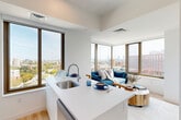 Located at 50 Western Avenue in Boston's Allston neighborhood, this thoughtfully designed two-bedroom, two-bathroom residence offers a bright, modern living experience. Light wood flooring and crisp white walls flow throughout, creating a clean, cohesive aesthetic across every room.

The open-concept kitchen and living area serves as the heart of the home, featuring sleek white cabinetry, stainless steel appliances including a range and dishwasher, and a peninsula with bar seating. Large floor-to-ceiling windows frame sweeping panoramic views of the Boston skyline and surrounding neighborhoods, flooding the space with natural light. The adjoining living and dining area benefits from corner windows that further extend the city views.

Both bedrooms are well-proportioned and serene, featuring light wood floors, large windows with city outlooks, and dedicated closets. The primary bedroom includes a louvered-door closet and ample wall space. The two bathrooms are finished in crisp white tile, with one featuring a full soaking tub and shower combination with contemporary chrome fixtures.

A hallway connects the main living spaces and provides access to a convenient in-unit laundry closet, housing a full-size stacked washer and dryer. Two additional closets offer generous storage throughout the residence.