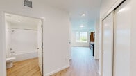 Located at 1145 SW 170th Ave in Beaverton, Oregon, this thoughtfully designed one-bedroom, one-bathroom apartment offers a clean, contemporary aesthetic throughout its efficiently arranged single-floor layout. Light wood-tone flooring runs continuously across all rooms, creating a cohesive and warm feel.

The open-concept kitchen and living area serves as the heart of the unit. The kitchen is outfitted with warm wood-toned cabinetry, white subway tile backsplash, a stainless steel refrigerator, dishwasher, range, and over-the-range microwave. A large picture window floods this space with natural light and frames views of the surrounding neighborhood and greenery.

The bedroom is a well-proportioned, bright retreat featuring a large window with outdoor views of the tree-lined streetscape below, a wall-mounted HVAC unit for personalized climate control, and a closet. The clean white walls and light flooring lend the room an airy, versatile character.

The bathroom includes a full tub-shower combination with a curved curtain rod, a wood-cabinet vanity with a white countertop, and wood-look flooring that ties the room to the rest of the unit. A hallway connects the main living area to the private spaces, completing the functional and modern floor plan.