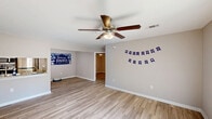 Located on Deloach Ave in Garden City, Georgia, this well-appointed single-story home offers a comfortable and functional layout across three bedrooms, two bathrooms, a kitchen, and a dedicated laundry room. The interior is finished with light wood-look luxury vinyl plank flooring throughout, creating a cohesive and easy-to-maintain aesthetic in every room. Neutral gray walls provide a clean, modern backdrop that complements the bright, airy feel of the space. The open living room is bathed in natural light from large windows with vertical blinds and features a ceiling fan with integrated lighting — a detail repeated across all bedrooms. The galley-style kitchen is well-equipped with white shaker cabinetry accented by matte black hardware, granite-look countertops, a stainless steel refrigerator, microwave, and electric range. The primary bedroom offers generous proportions with natural light filtering through a window with blinds. Both bathrooms are neatly appointed, one featuring a vanity with a granite-look countertop, white cabinetry, a framed mirror, and brushed nickel fixtures. The dedicated laundry room accommodates a full-size washer and dryer with built-in shelving above. Three closets provide ample storage throughout the home.