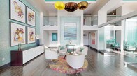 This contemporary space makes an immediate impression with its dramatic double-height ceilings and open, airy design. The main living area is anchored by a striking cluster of sculptural pendant lights — featuring yellow, brown, and bronze tones — that hang as artistic focal points above a curated seating arrangement. Four sleek white swivel chairs surround a glass coffee table, all set atop a vivid, multicolored circular rug that adds a bold splash of warmth and energy to the refined space.

The walls are adorned with carefully selected artwork, complementing the soft aqua and teal accent tones that appear throughout, including a shimmering mosaic tile feature wall framing a large abstract painting. Clean white walls and wide-plank hardwood-style flooring provide a neutral backdrop that allows the colorful design elements to truly stand out.

A glass-railed upper-level overlook adds architectural depth and visual interest, enhancing the sense of vertical space. Natural light flows generously throughout, further brightening the interior. A sleek white credenza along one wall provides functional storage while maintaining the space's polished aesthetic. Overall, the space exudes a modern, gallery-like ambiance with a sophisticated yet approachable character.