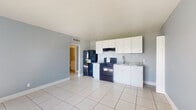 Located at 1001 36th St in West Palm Beach, FL, this single-floor unit offers a clean and functional layout designed for comfortable everyday living. The interior is finished with large-format light tile flooring throughout, soft blue-gray painted walls, and crisp white baseboards that give the space a bright, cohesive aesthetic.

The open living and kitchen area forms the heart of the unit. The kitchen is equipped with white shaker-style cabinetry extending to the upper walls for generous storage, granite-look countertops, a stainless steel sink, and black appliances including a gas range and a full-size refrigerator. A range hood is mounted above the stove, and a subtle tile backsplash adds a polished touch. Natural light pours into the adjoining living area through a large window, creating an airy atmosphere.

The bedroom is a well-proportioned room with the same tile flooring and neutral wall tones. It features a wide reach-in closet enclosed by louvered bi-fold doors, providing ample storage space.

The bathroom includes a full tub-shower combination with floor-to-ceiling beige marble-style tile surround, a white vanity with granite countertop, and a clean, understated design. Central air conditioning is present throughout the unit, with visible ceiling vents ensuring consistent climate control.