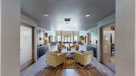 Located at 1659 Drew Ave in Davis, CA, this generously sized amenity space at Octave Davis offers residents a well-rounded collection of shared facilities across a single floor. The welcoming entrance opens into an elegantly appointed lounge area, where light wood-style flooring, vibrant abstract artwork, and a curated seating arrangement of textured swivel chairs create an inviting atmosphere ideal for socializing or relaxing. The living room extends into a dramatic double-height great room with soaring ceilings, exposed beams, and expansive windows that flood the space with natural light and offer views of the outdoor pool area. A full-sized billiards table anchors this central gathering space. The kitchen is outfitted with sleek gray shaker cabinetry, stainless steel appliances, a geometric 3D tile backsplash, and ample counter space, making it well-suited for community events. The fitness center is divided into two well-equipped zones: one featuring strength training machines with floor-to-ceiling mirrors and direct outdoor access, and another with treadmills, a wall-mounted TV, and natural light from large windows. A clean, ADA-accessible bathroom with wood-look flooring and a package locker room with a full wall of secure lockers round out the functional offerings of this thoughtfully designed community space.