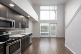 This two-story residence offers a thoughtfully designed layout that maximizes both space and functionality. The main floor centers around an open-concept living area distinguished by dramatic double-height ceilings and floor-to-ceiling windows with sliding glass doors that flood the interior with abundant natural light and provide outdoor access. Rich, dark hardwood-style flooring runs throughout the main level, complementing the contemporary aesthetic. The kitchen is efficiently designed along a single wall and features dark espresso cabinetry with sleek hardware, white quartz countertops, a subway tile backsplash, and a full suite of stainless steel appliances including a range, over-the-range microwave, dishwasher, and refrigerator. A staircase with a clean white railing connects the main floor to the upper level. The second floor offers a spacious bedroom with a built-in double-door closet and warm wood-style flooring. The bathroom includes a dark vanity with a white countertop and single sink, a large mirror, a shower, and accessible grab bars for added convenience. Throughout the residence, neutral wall tones and recessed lighting create a calm, cohesive ambiance well-suited for modern living.