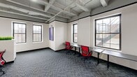 Located in the heart of downtown Pontiac, Michigan, this thoughtfully designed office suite blends industrial character with contemporary finishes across a single floor. Exposed concrete coffered ceilings and painted structural beams lend an urban, loft-like aesthetic throughout the open common areas, while herringbone hardwood flooring adds warmth and sophistication to the lounge and reception zones.

The suite features multiple private offices and workrooms, each outfitted with patterned carpet tiles, sleek light-toned desks, and black-framed glass partition doors that maintain visual connectivity without sacrificing privacy. Bold motivational artwork — including vivid "HUSTLE" and "WORK HARD. PLAY HARD." wall pieces — energizes the workspace with an entrepreneurial spirit.

A welcoming lounge area provides comfortable seating arrangements with neutral-toned chairs and a round coffee table, bathed in natural light from large, multi-pane windows that frame views of the surrounding downtown streetscape. A kitchenette featuring dark wood cabinetry, gold hardware, open shelving, and a beverage refrigerator serves as a functional hub for the suite.

The media room and a dedicated recreation lounge — complete with a pool table and plush seating — round out the amenities, creating a well-balanced environment designed to support both focused productivity and collaborative engagement.