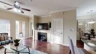 This single-floor residence offers a thoughtfully designed open-concept layout that seamlessly connects the kitchen, dining, and living areas. The kitchen is outfitted with rich, dark espresso cabinetry extending to the ceiling, dark granite countertops, black appliances including a refrigerator, electric range, and built-in microwave, and a multi-seat breakfast bar with pendant lighting overhead. Crown molding throughout adds a polished architectural detail.

The living room is bright and inviting, featuring warm hardwood-style flooring, a ceiling fan, and large windows with horizontal blinds that allow generous natural light. A fireplace with a classic white mantle serves as a focal point, and a sliding glass door leads to a private balcony with views of the surrounding area. An adjacent dining area accommodates a full-sized table beneath a pendant light fixture.

The bedrooms are carpeted and comfortably sized, each equipped with a ceiling fan and windows that bring in natural light. The bathroom features dark cabinetry, granite countertops, a dark-framed mirror, and a tub-shower combination. The entryway transitions smoothly from the front door into the kitchen and main living spaces, creating a cohesive and functional flow throughout the home.